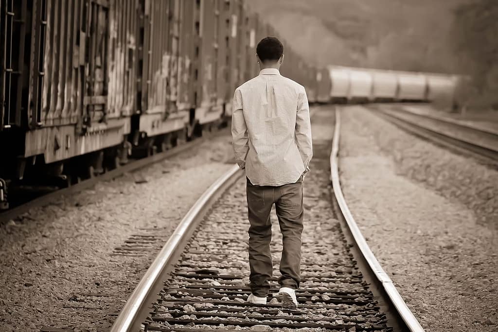 A sepia image of a man walking away down railroad tracks